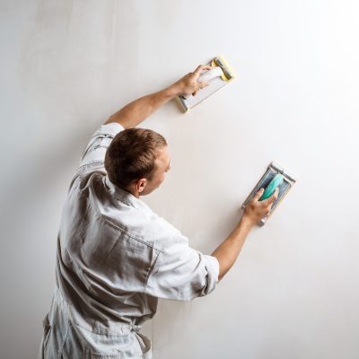 Professional worker grinding white wall with sandpaper. Copy space.
